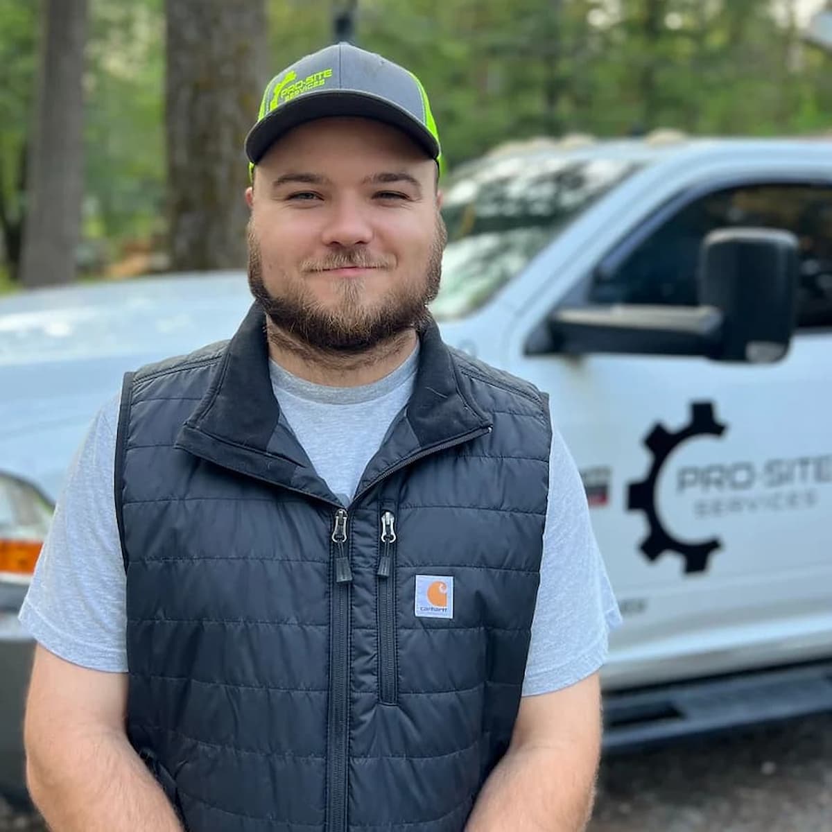 Jordan berry owner operator of pro-site services, standing facing camera wearing green hat smiling at camera with work truck in background.